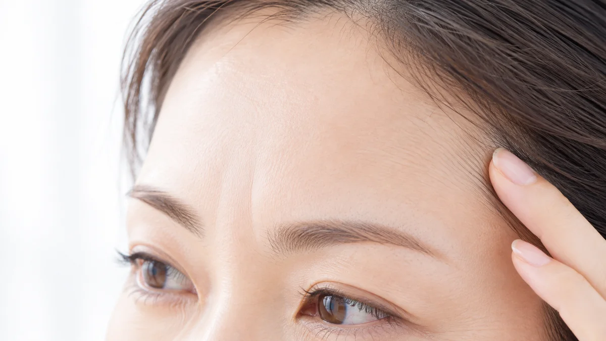 おでこ・眉間・こめかみのイメージ写真。こめかみに指先を添えた女性の、額と目元