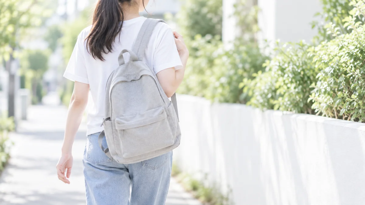 リュックを背負って並木道を歩く10代の女性の後ろ姿のイメージ写真