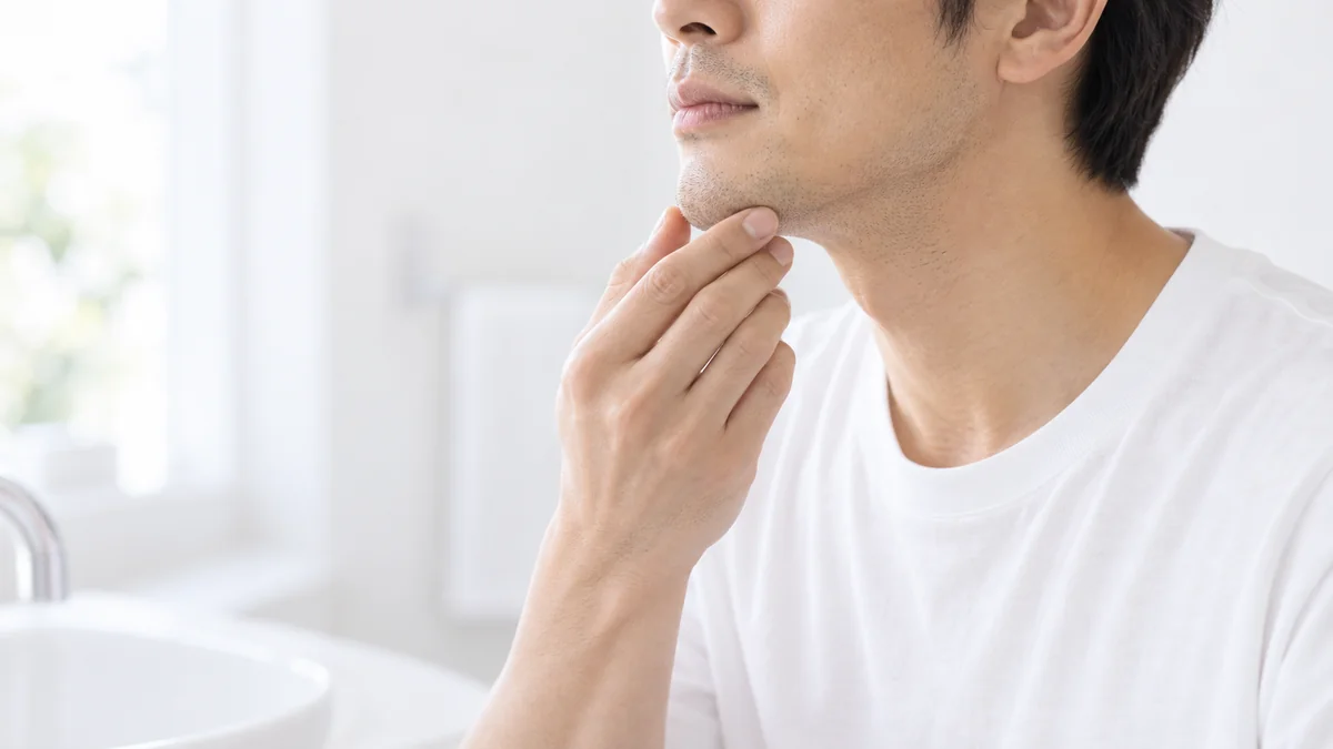白いTシャツの男性が、あごにそっと手を添えるイメージ写真