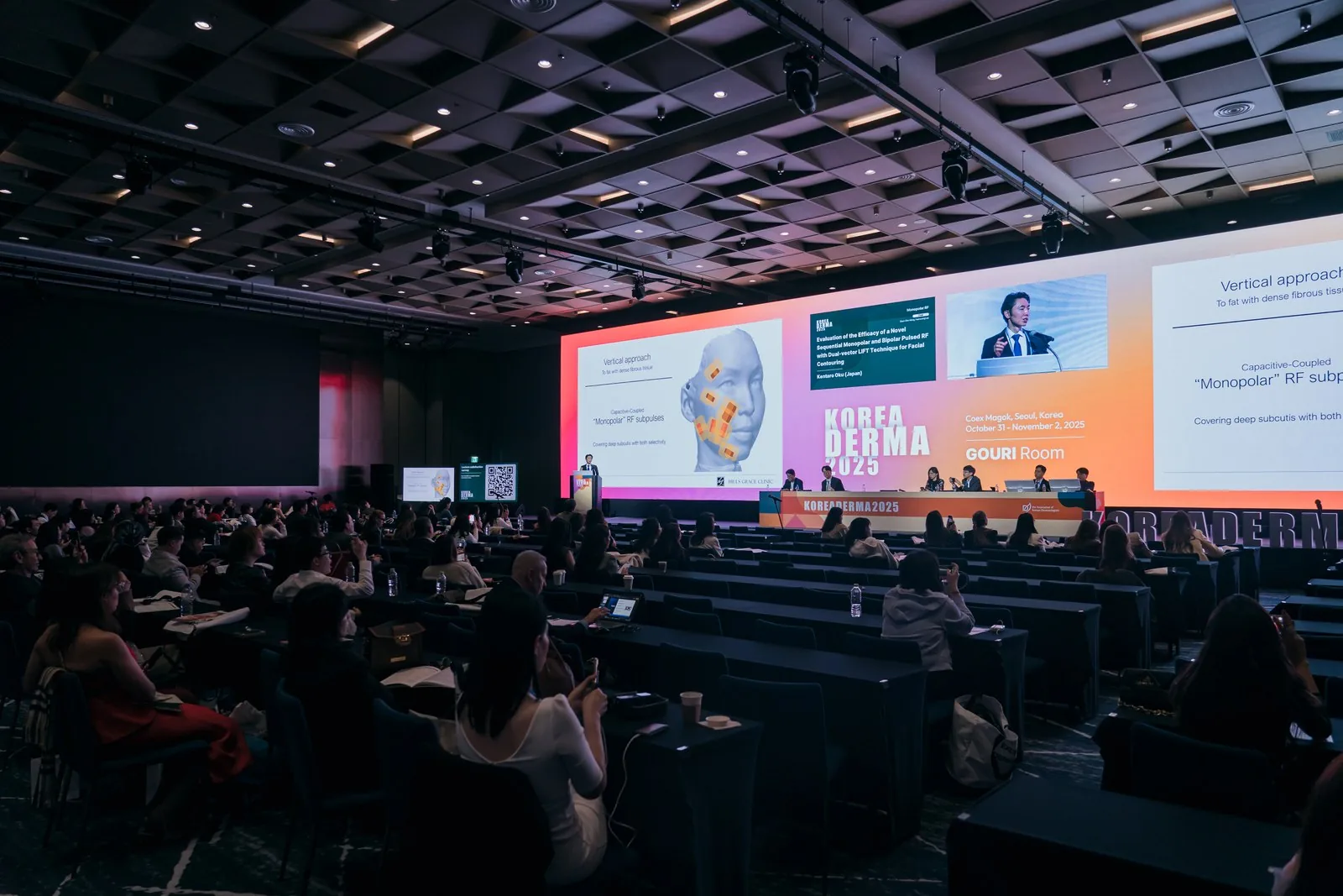 KOREA DERMA 2025の大会場で、モノポーラーRFの熱の向きを示すスライドを使って講演する院長 奥謙太郎